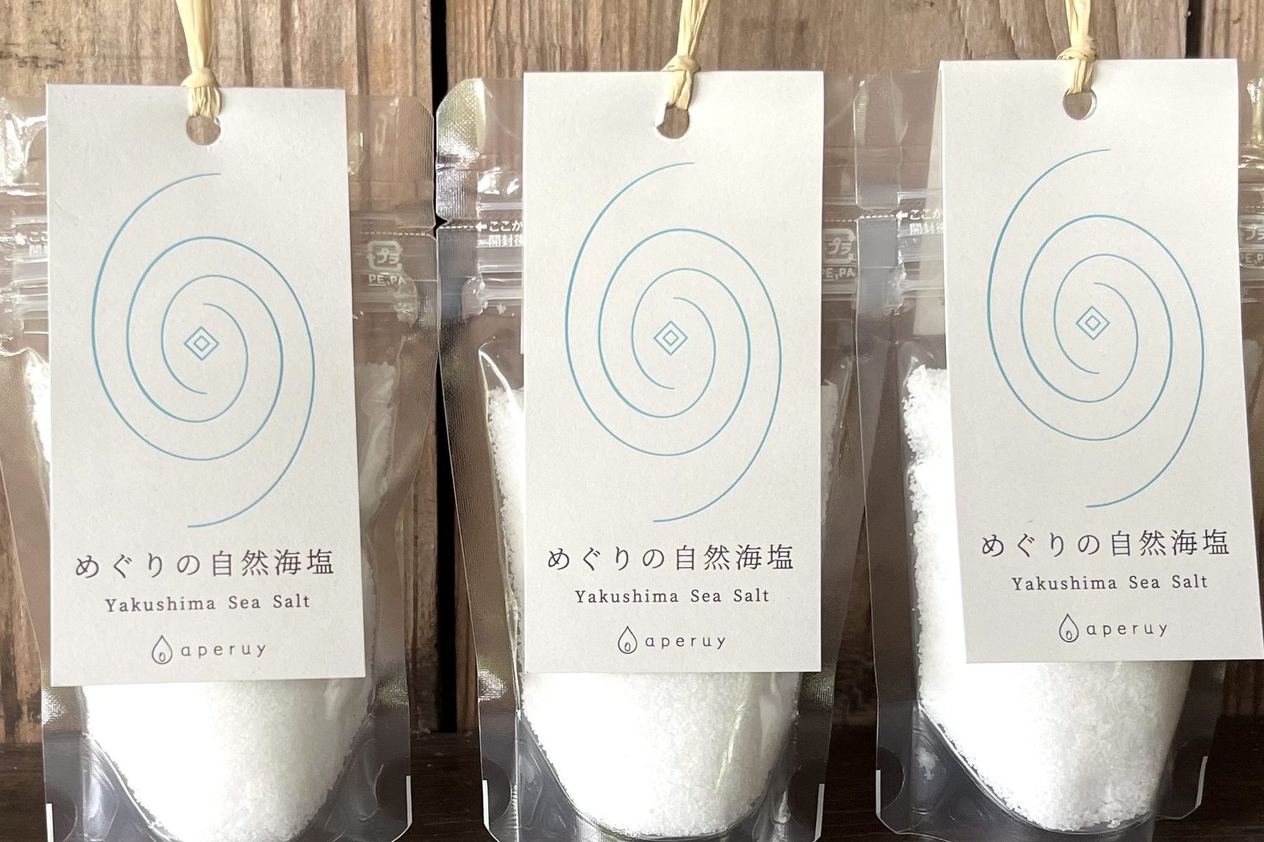 木の壁の前に並ぶ、めぐりの自然海塩のパッケージ